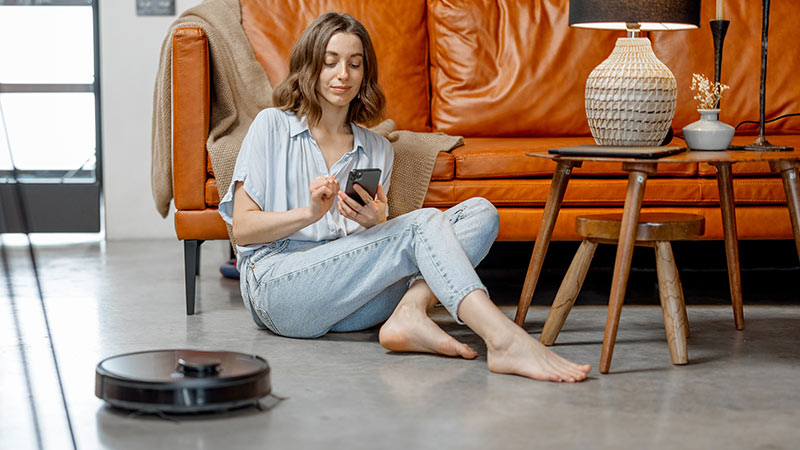 Rapariga com telemóvel e aspirador robô